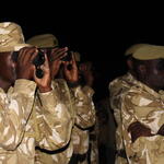 Night shot of men in camoflauge uniforms sitting down and looking through night vision binoculars