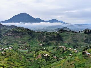 Rolling green hills with homes on them and large cloud-covered mountains in the background