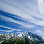 Tall mountains with blue sky above. White vapor trails streak across the blue sky. 