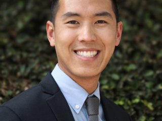 Alex Yee smiles, wearing a suit and tie.