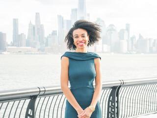 Alexa White stands in front of a river and city skyline smiling at the camera