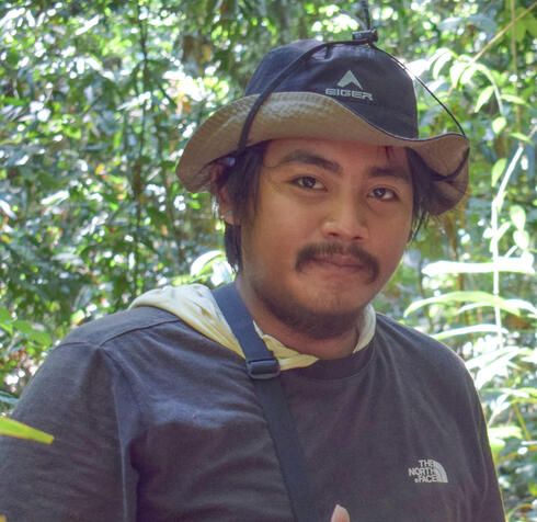 Alfred Indra Kusuma Rombe stands in the forest looking at the camera with a smile.