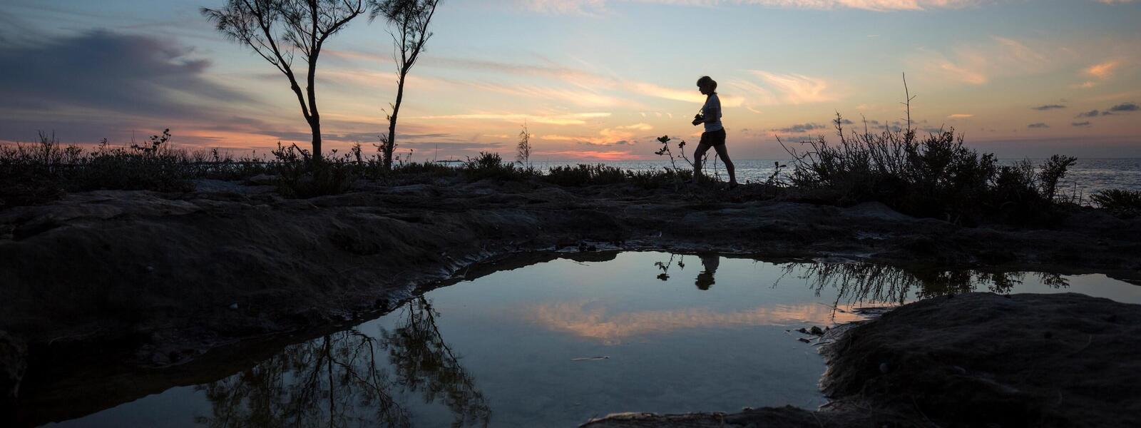 WWF staff person walks at dusk with tidepools in the foreground and ocean in the background