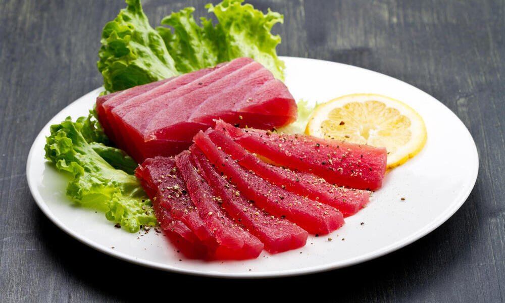Slices of raw bluefin tuna sashimi on a plate with a lemon slice