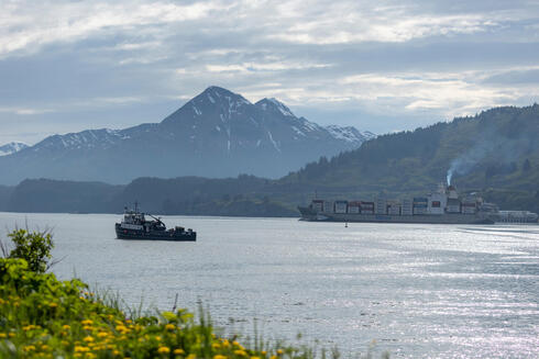 Fishing boat and container ship in a harbor with mountains in background