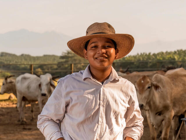 A young man smiling at camera with cattle in background