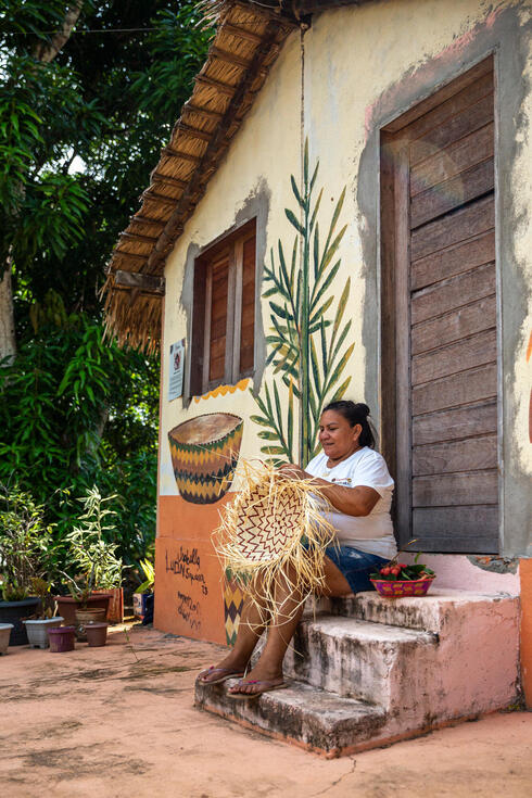 A woman weaving while sitting on a step outside a house