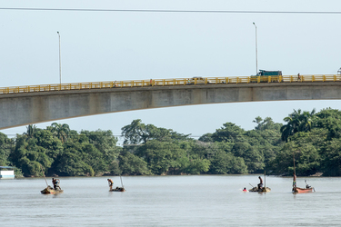 Men fishing in small boats beneath modern bridge