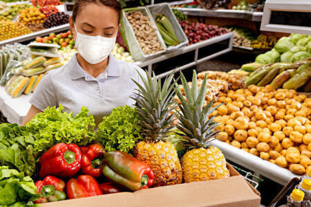 Masked person holding box of colorful produce