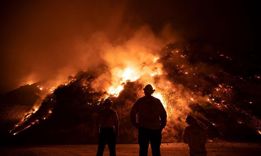 Firefighters fight a large fire burning in the hills.