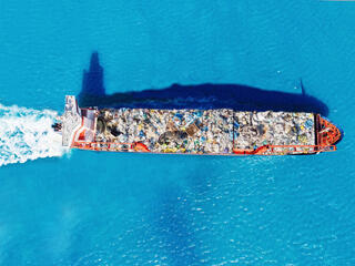 Aerial view of a cargo ship transports containers of garbage across blue waters for recycling factory.