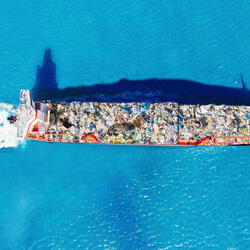 Aerial view of a cargo ship transports containers of garbage across blue waters for recycling factory. 
