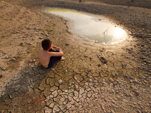 A child sits on cracked earth near drying water.