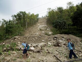 Two children walk in front of a steep dirt slope after a landslide