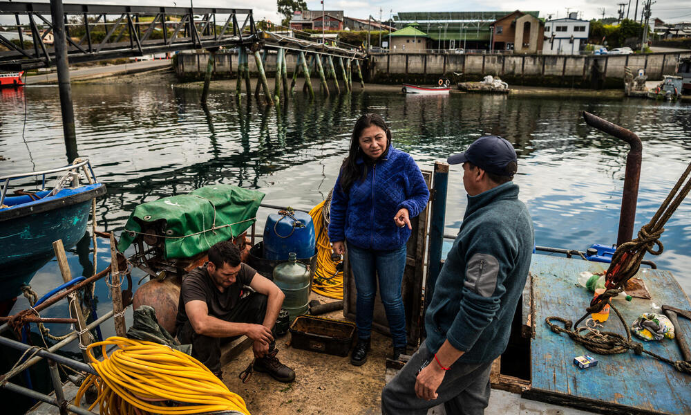 A fisherwoman speaks to 2 men on deck