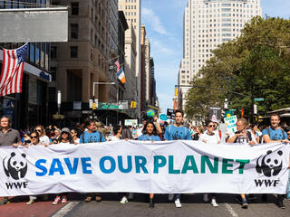People marching down a New York City street holding "Save Our Planet" banner