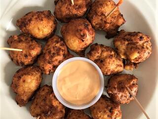 A plate of conch fritters with dipping sauce in the center
