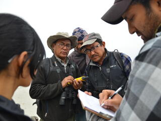 A man writes in a notebook while a group of people stand and observe