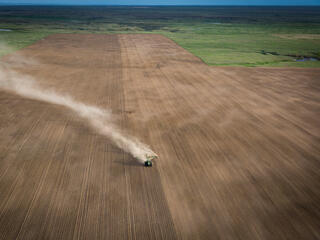 An aerial view of a tractor kicking up dust as it drives across converted grassland