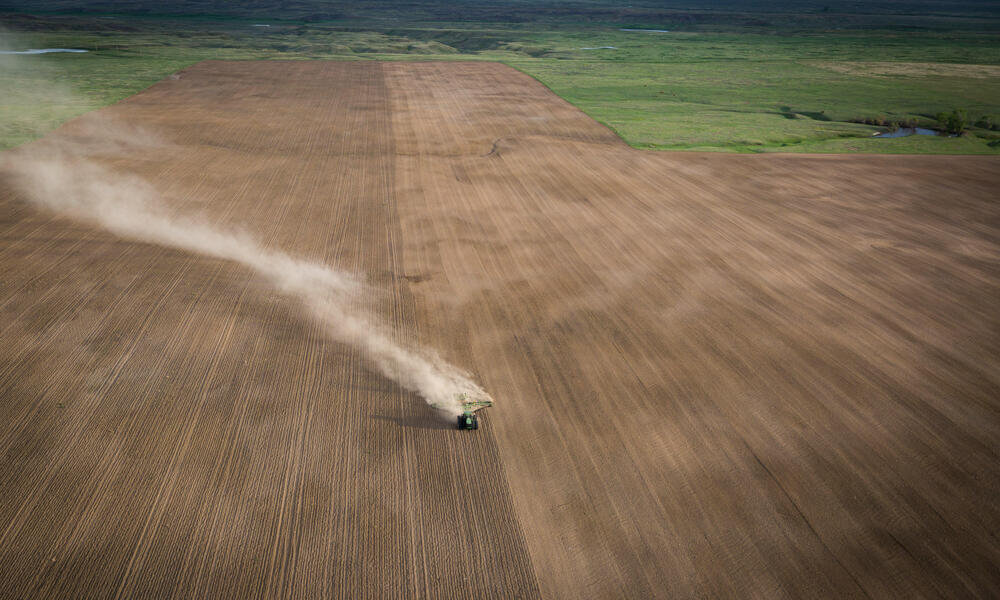 An aerial view of a tractor kicking up dust as it drives across converted grassland