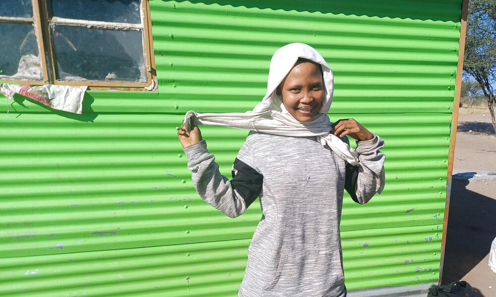 Portrait of a Nama Pan villager in front of a green tin wall