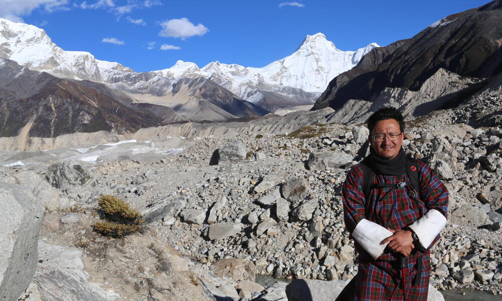 Dechen Dorji stands in front of tall snowy peaks on a sunny day