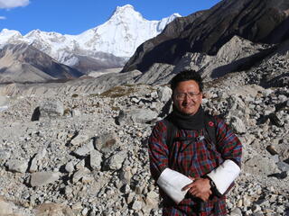 Dechen Dorji stands in front of tall snowy peaks on a sunny day