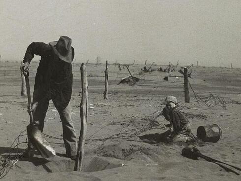 Dust bowl farmer raising fence to keep it from being buried under drifting sand