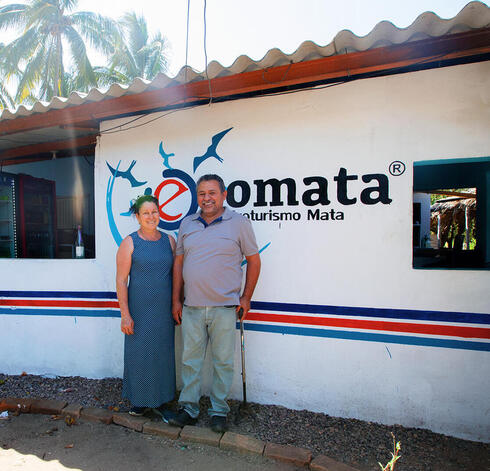 Couple stands in front of building with sign Ecomata