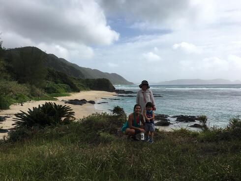 Ellie Yanagisawa kneels next to her nephew. Her grandma stands behind them. They all are on a beach in Amami.