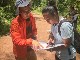 Two researchers stand in a Borneo forest looking over notes on a pad of paper