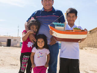 A man stands with his three children, two girls and a boy holding a large toy boat, all smiling looking at the camera