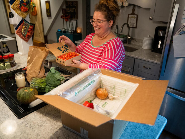 A person opens a box of fresh produce on her kitchen counter