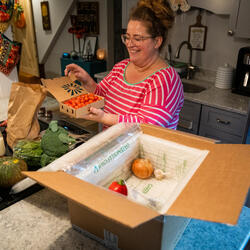 A person opens a box of fresh produce on her kitchen counter