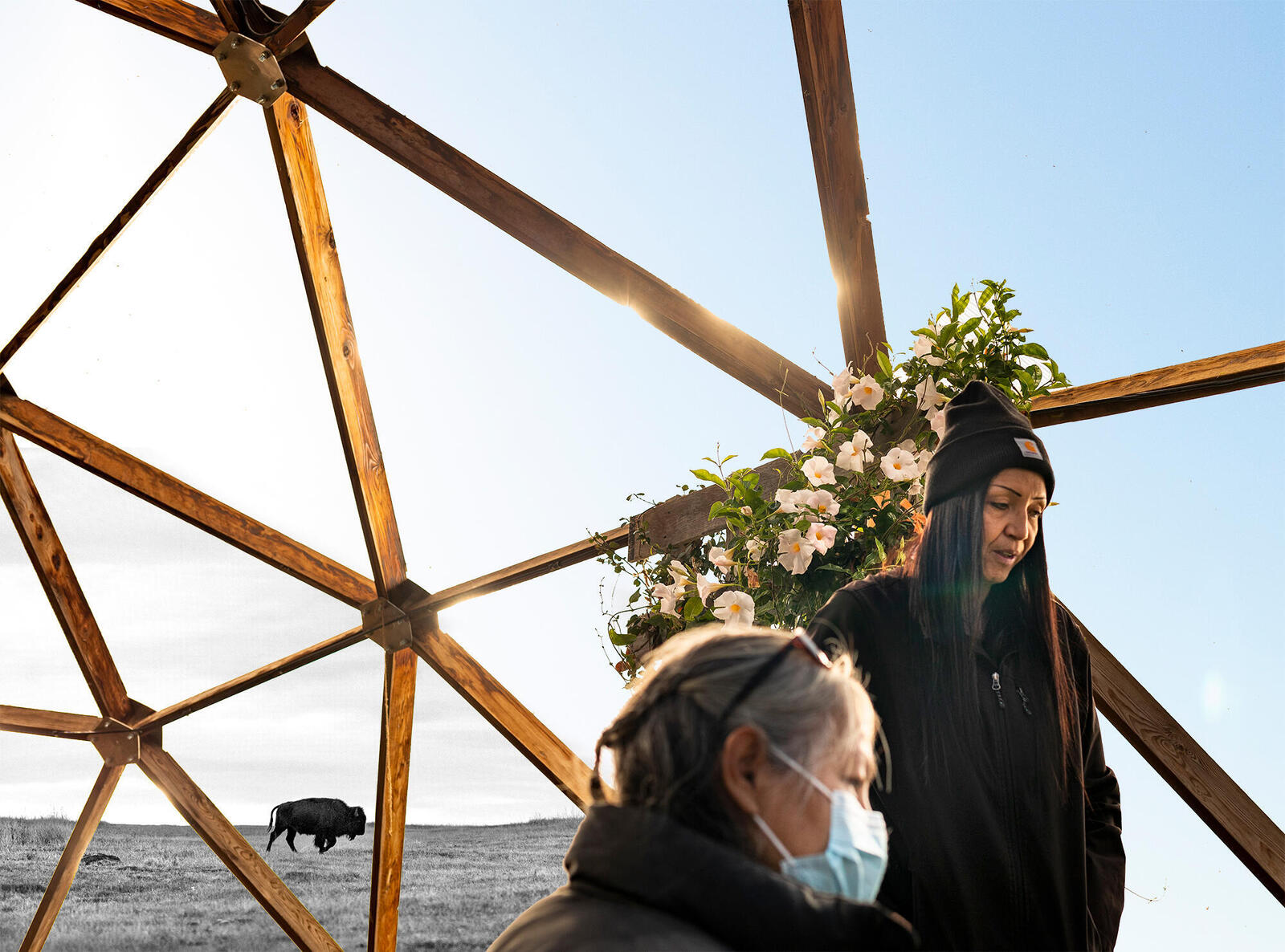 Two women looking at plants under a greenhouse frame
