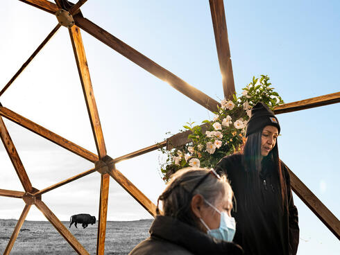 Two women looking at plants under a greenhouse frame