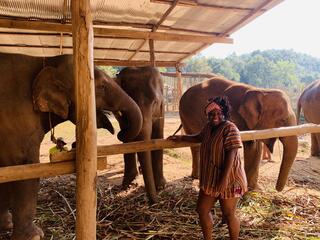 Florence Adewale stands in front of a group of elephants gathered under a roof 