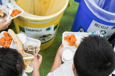 children hold trays over barrels intended to compost food