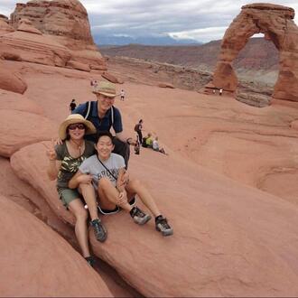 Grace Lee sits in front of her mom and dad at a national park with a huge red arch in the background