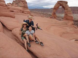 Grace Lee sits in front of her mom and dad at a national park with a huge red arch in the background