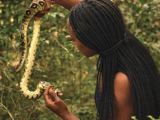 Woman in braids holding a yellow snake up