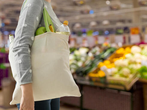 A woman with a beige tote bag walks through the produce section of a grocery store