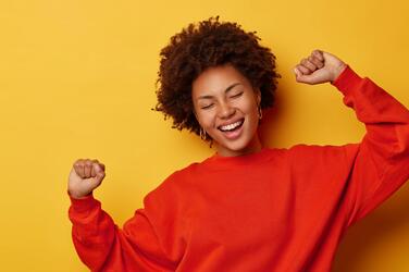 Woman celebrates with her eyes closed and her hands up against a solid background