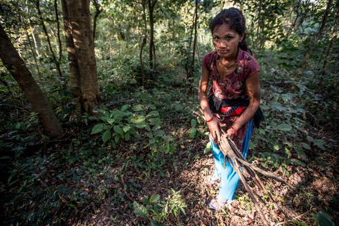 A woman carrying sticks in the forest looks up at the camera
