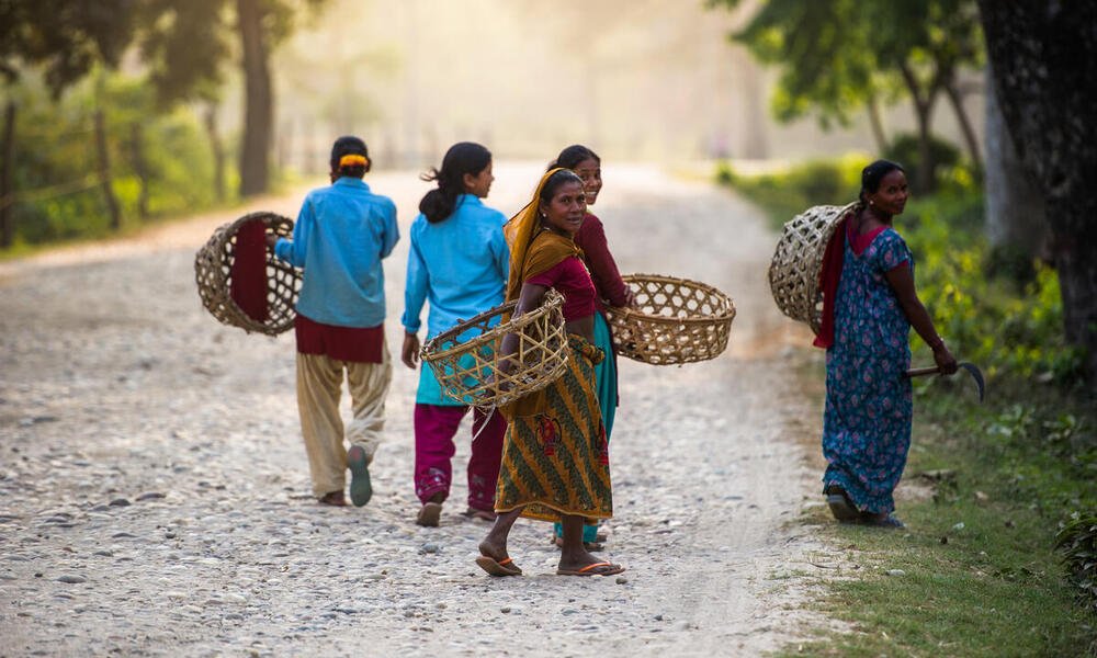 Women carry baskets and wear colorful clothes as they walk down a path