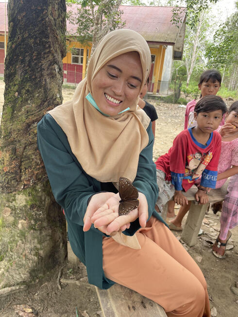 Herni holds a moth in her hands and smiles at it