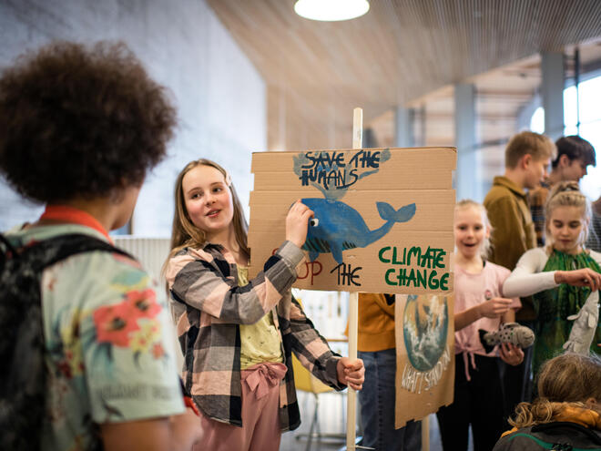 A young girl holds up a cardboard sign with a whale that says "Save the humans" and "Stop the climate change"
