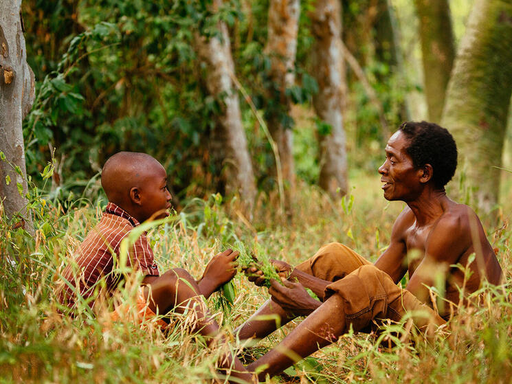 An older man and a younger man sitting in a forest talking