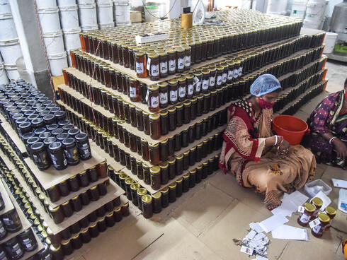 Women sit in front of a large stack of full honey jars ready for shipment
