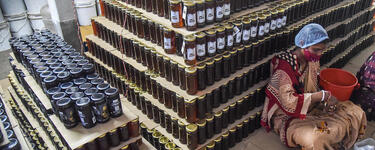 Women labeling stacks of honey in jars in warehouse